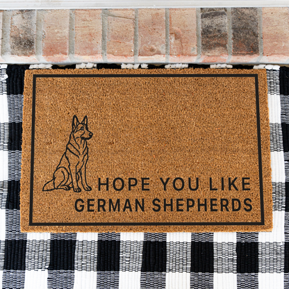Hope You Like German Shepherds coir doormat with a drawing of a sitting German shepherd on a black and white buffalo check rug, close view