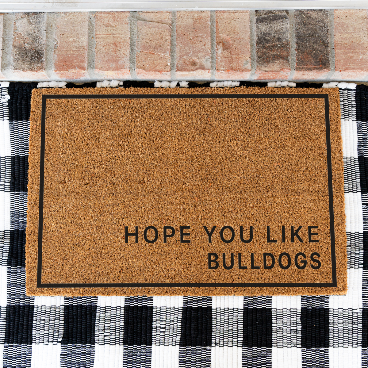 Hope You Like Bulldogs minimalist coir doormat with a thin black border on a black and white buffalo check rug, close view