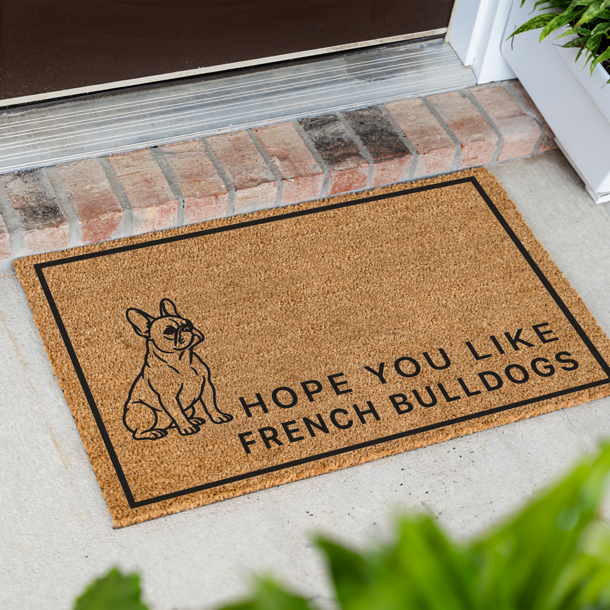 Hope You Like French Bulldogs coir doormat with a drawing of a sitting French bulldog at an angle on a front porch by a brick step