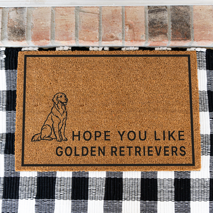 Hope You Like Golden Retrievers coir doormat with a drawing of a sitting golden retriever on a black and white buffalo check rug, close view