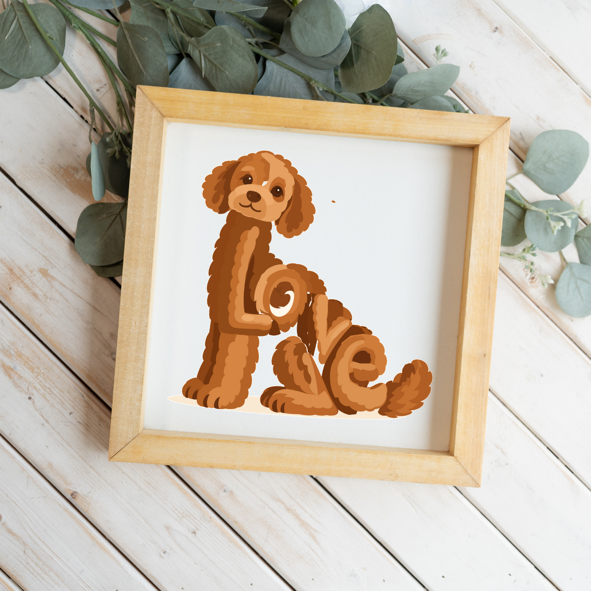 Sitting red doodle Love square framed sign with a natural wood frame on white wood planks with eucalyptus