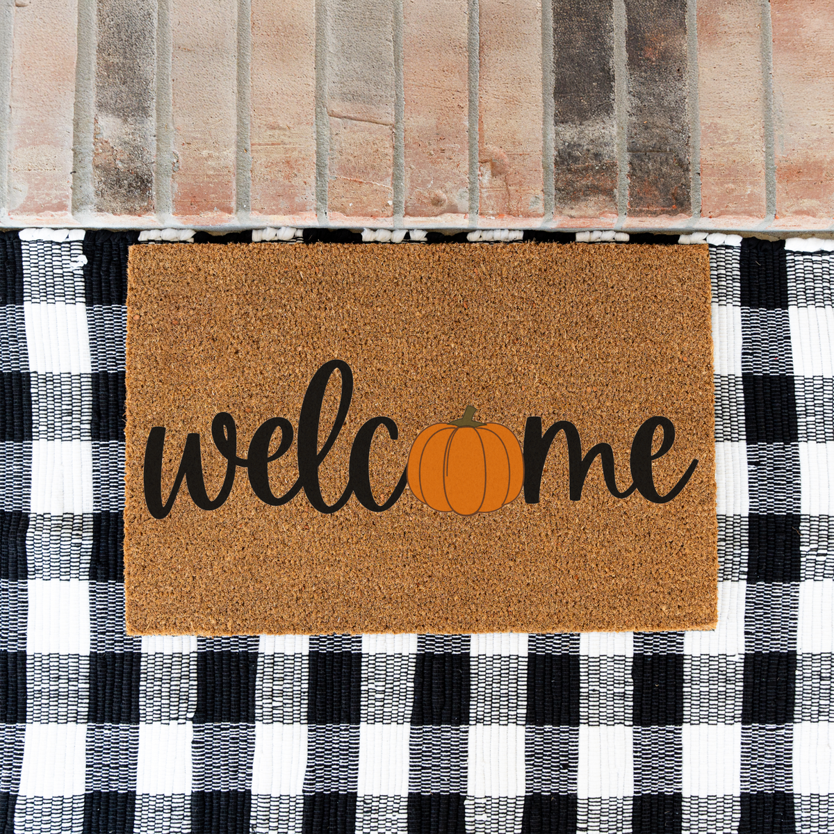 Welcome pumpkin coir doormat on a black and white buffalo check rug at a brick step