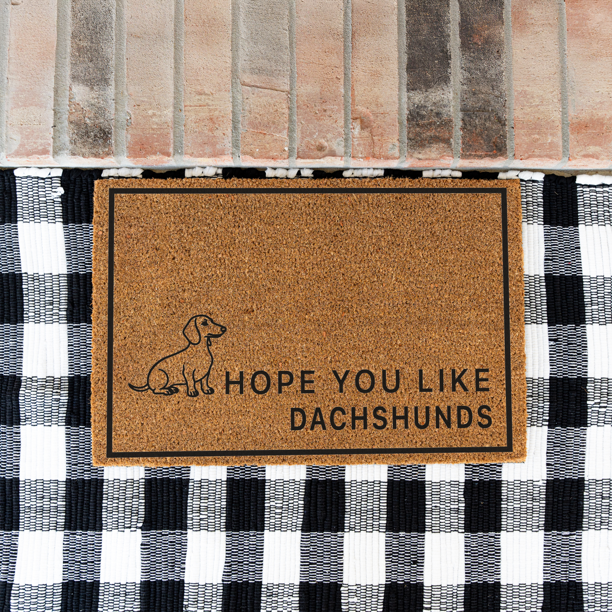 Hope You Like Dachshunds coir doormat with a drawing of a sitting dachshund on a black and white buffalo check rug at a brick step