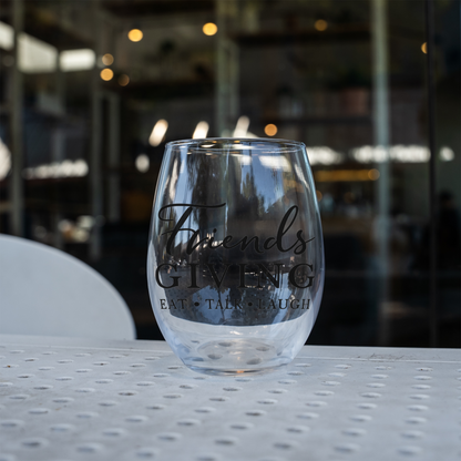 Friendsgiving stemless wine glass, empty, on a perforated metal patio table in front of a cafe window