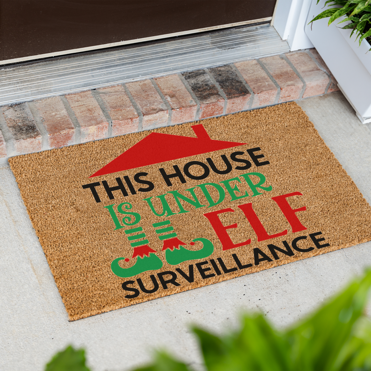 This House Is Under Elf Surveillance coir doormat at an angle in front of a brick step
