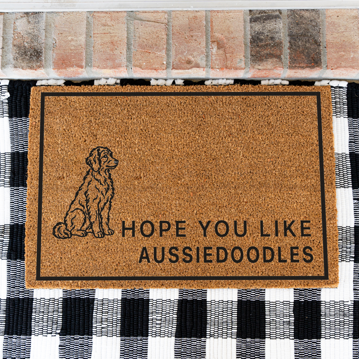 Hope You Like Aussiedoodles coir doormat with a drawing of a sitting Aussiedoodle on a black and white buffalo check rug, close view