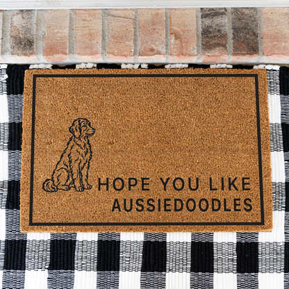 Hope You Like Aussiedoodles coir doormat with a drawing of a sitting Aussiedoodle on a black and white buffalo check rug, close view