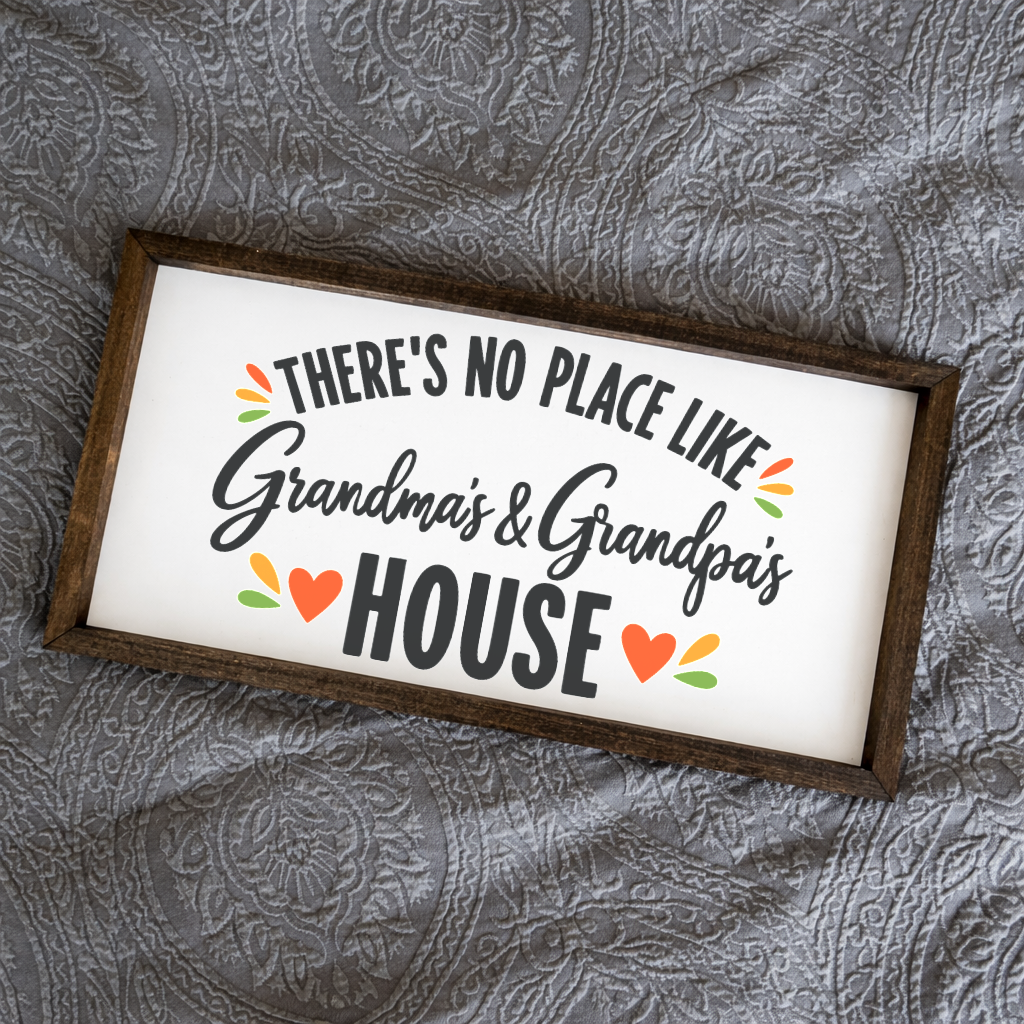 There's No Place Like Grandma's & Grandpa's House wide framed sign with a walnut frame on a grey quilted bedspread
