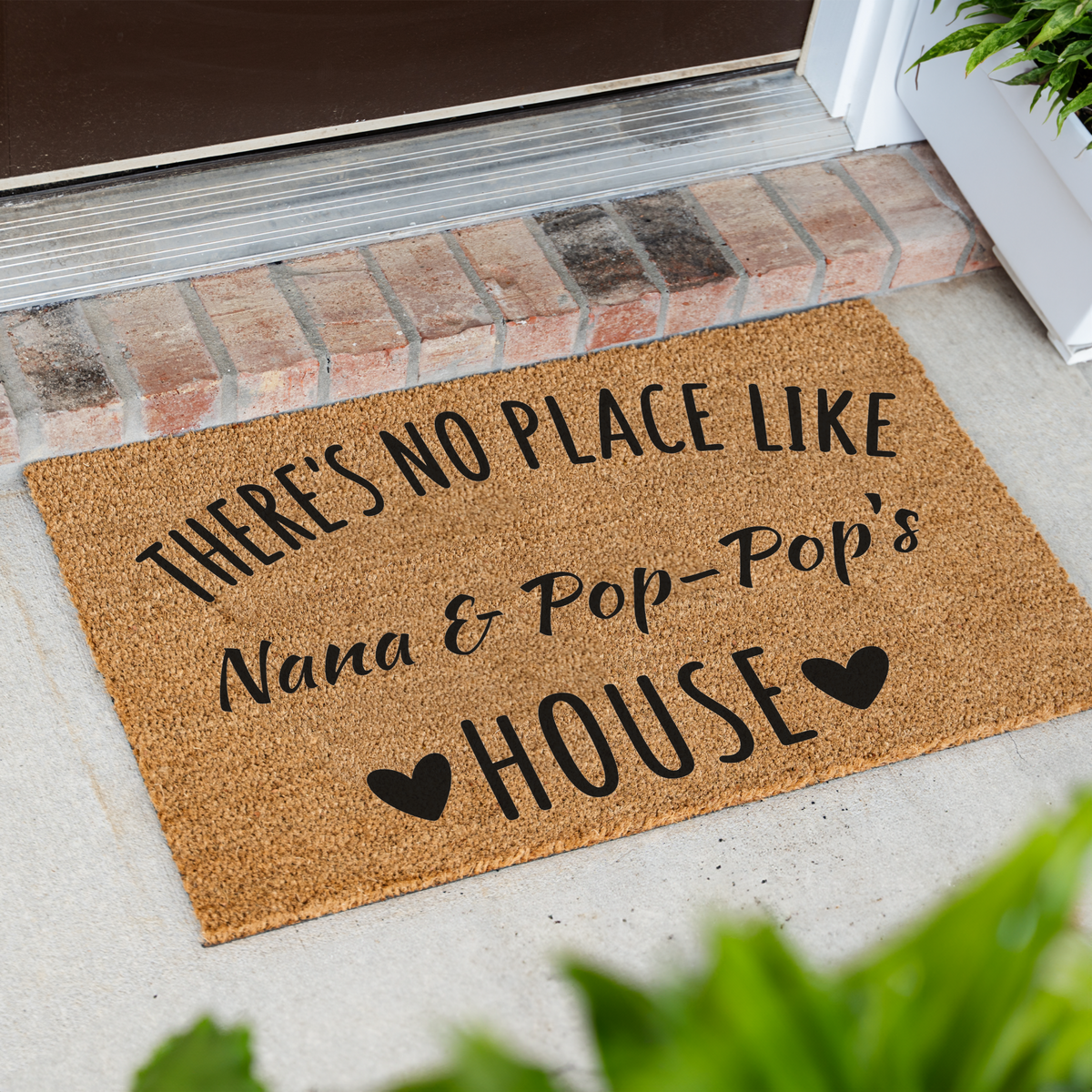 There's No Place Like Nana & Pop-Pop's House coir doormat at an angle on a front porch by a brick step