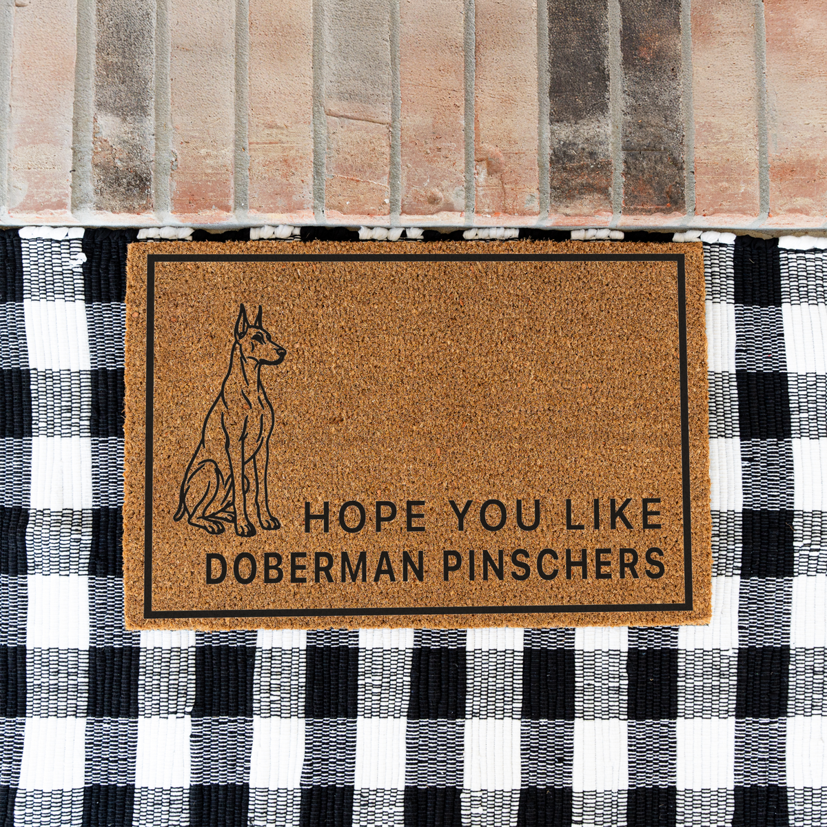 Hope You Like Doberman Pinschers coir doormat with a drawing of a sitting Doberman pinscher on a black and white buffalo check rug at a brick step