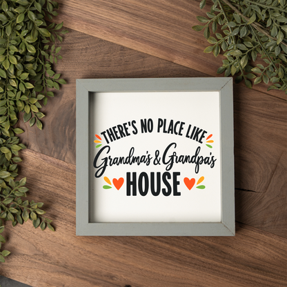 There's No Place Like Grandma's & Grandpa's House square framed sign with a grey frame on a dark wood table with greenery