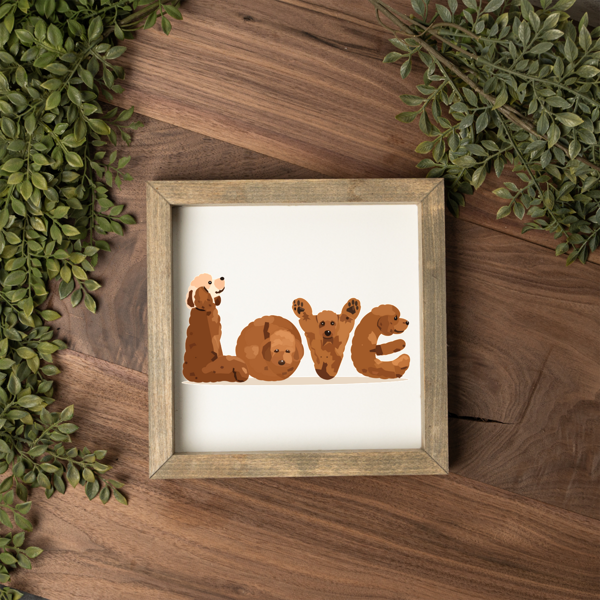 Four red doodles spelling LOVE square framed sign with a weathered wood frame on a dark wood table with greenery
