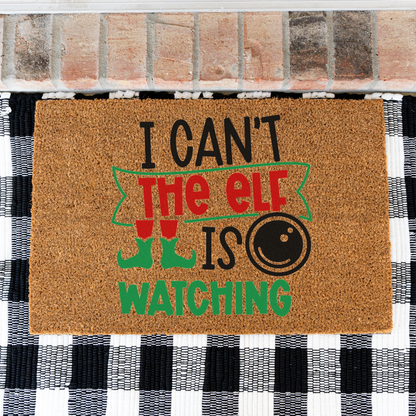 I Can't The Elf Is Watching coir doormat on a black and white buffalo check rug, close view