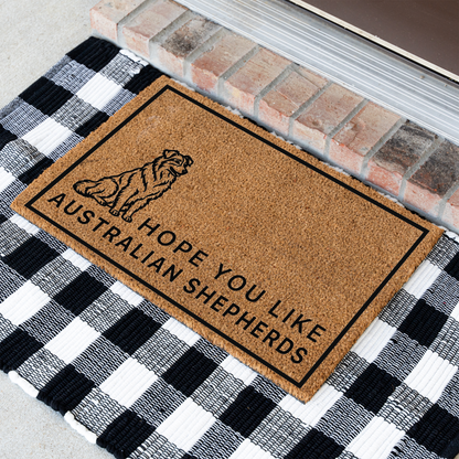 Hope You Like Australian Shepherds coir doormat with a drawing of a sitting Australian shepherd at an angle on a black and white buffalo check rug