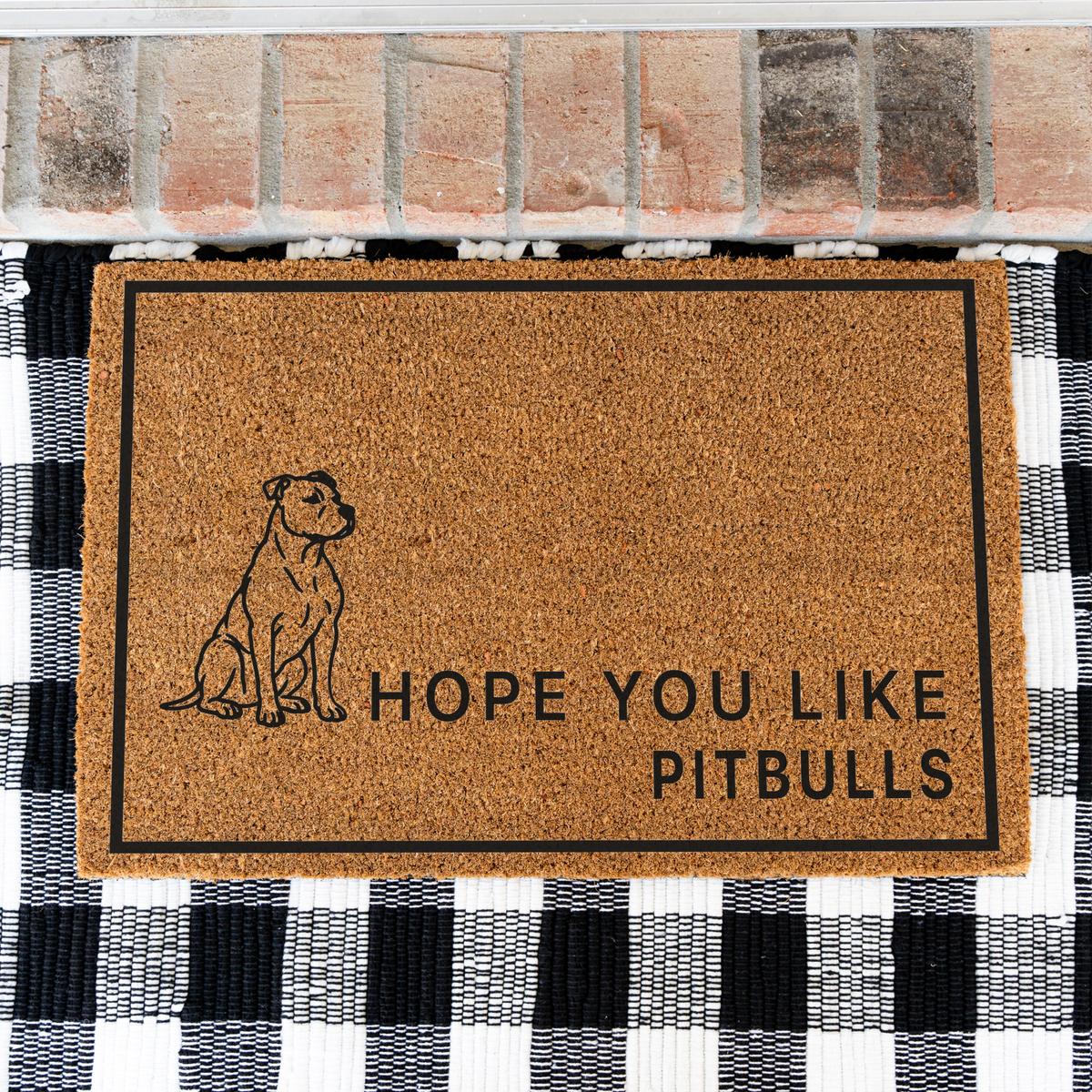 Hope You Like Pitbulls coir doormat with a drawing of a sitting pitbull on a black and white buffalo check rug, close view