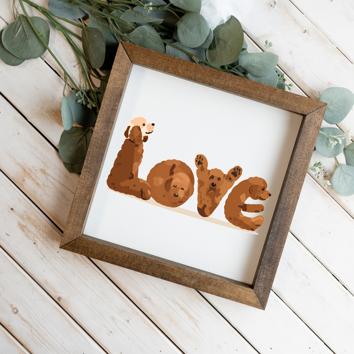 Four red doodles spelling LOVE square framed sign with a walnut frame on white wood planks with eucalyptus