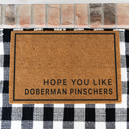 Hope You Like Doberman Pinschers minimalist coir doormat with a thin black border on a black and white buffalo check rug, close view