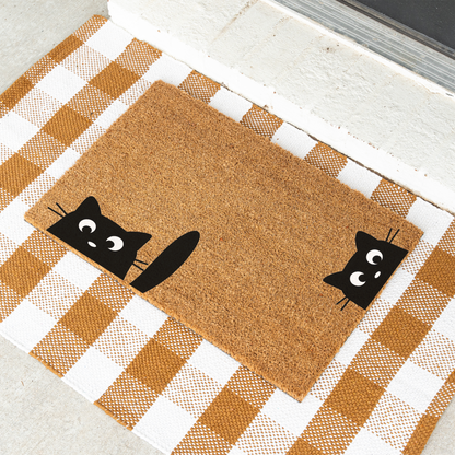 Peeking black cats coir doormat on a tan and white check rug