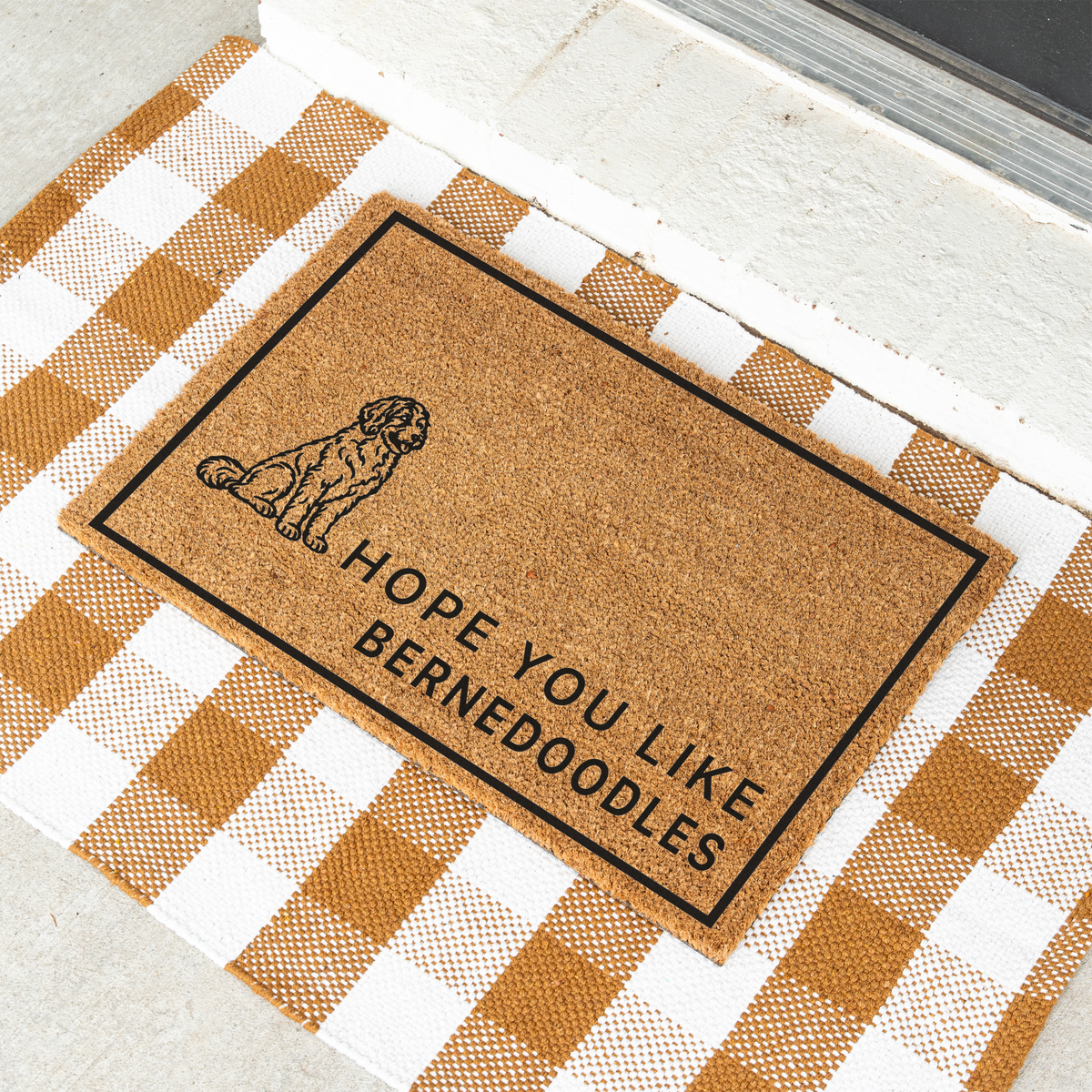 Hope You Like Bernedoodles coir doormat with a drawing of a sitting Bernedoodle at an angle on a tan and white check rug
