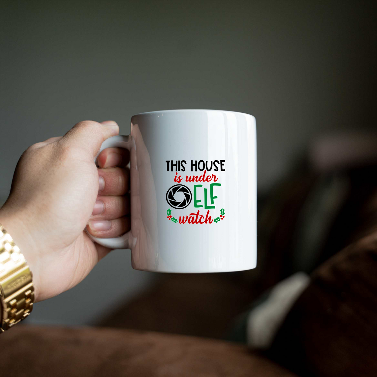 This House Is Under Elf Watch white ceramic Christmas coffee mug held in a hand