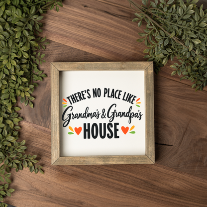 There's No Place Like Grandma's & Grandpa's House square framed sign with a weathered wood frame on a dark wood table with greenery