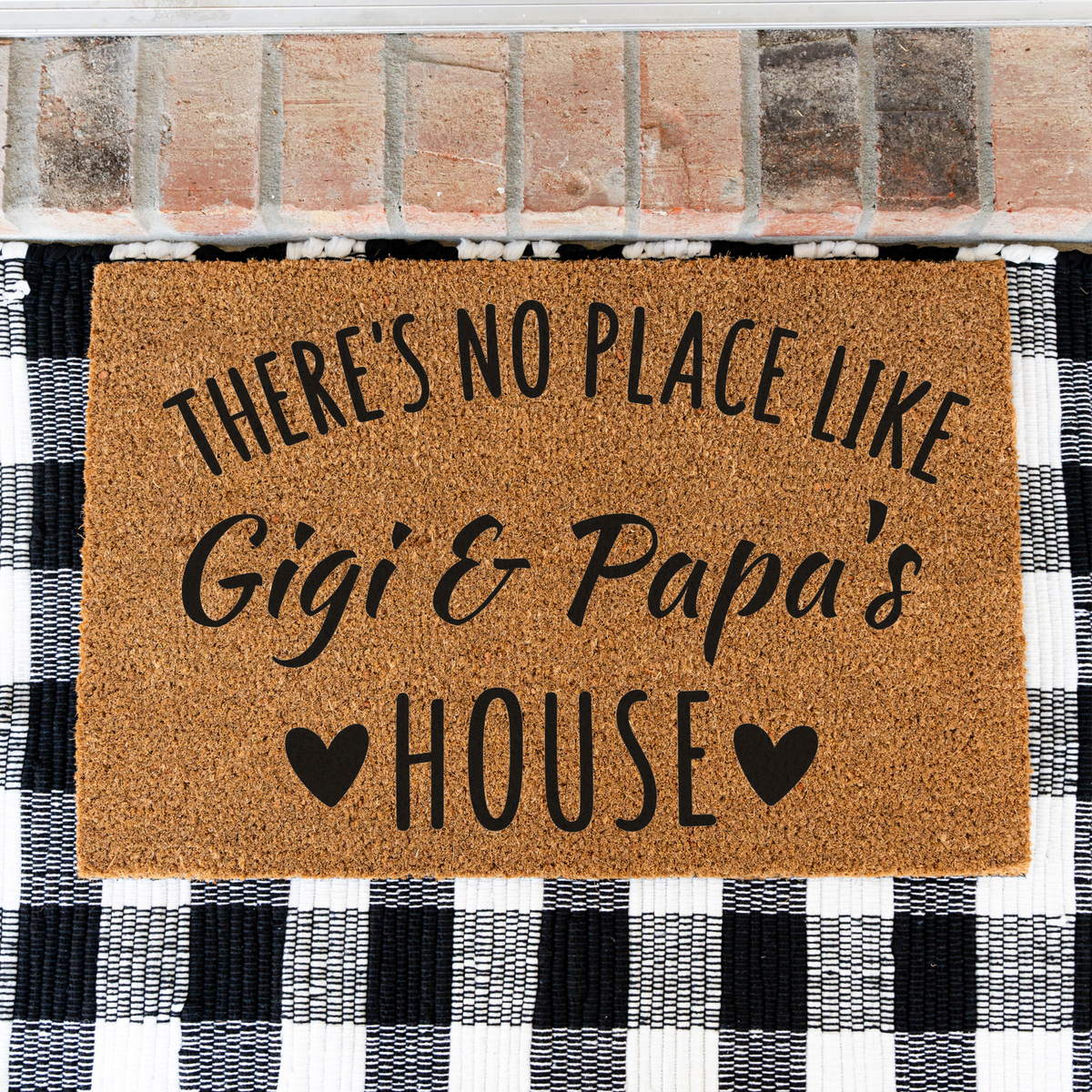 There's No Place Like Gigi & Papa's House coir doormat on a black and white buffalo check rug, close view