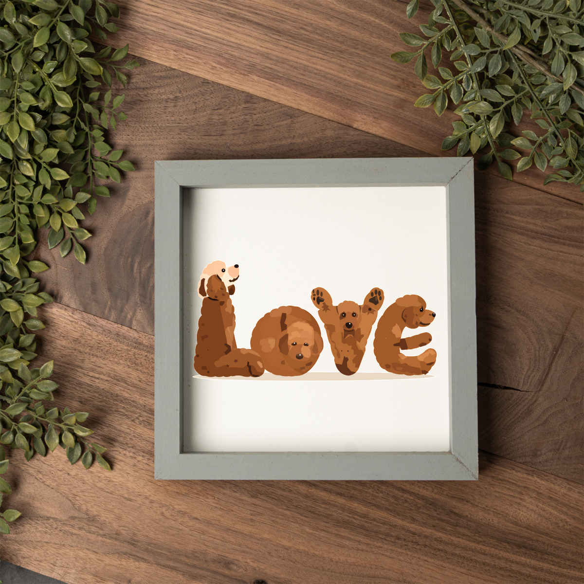 Four red doodles spelling LOVE square framed sign with a grey frame on a dark wood table with greenery