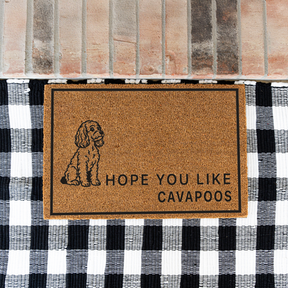 Hope You Like Cavapoos coir doormat with a drawing of a sitting Cavapoo on a black and white buffalo check rug at a brick step