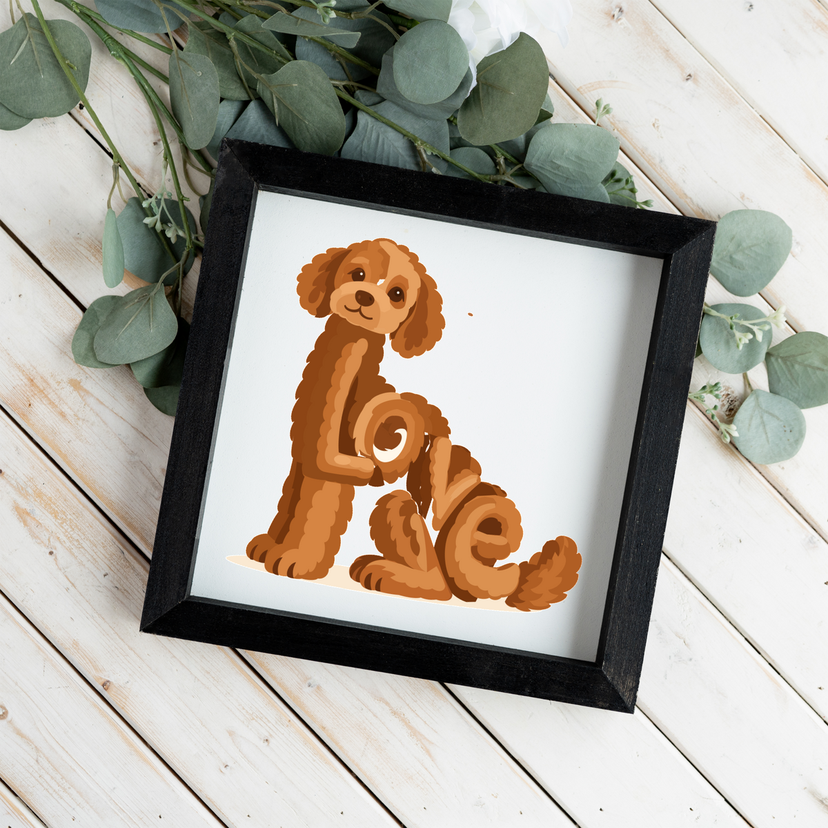 Sitting red doodle Love square framed sign with a black frame on white wood planks with eucalyptus