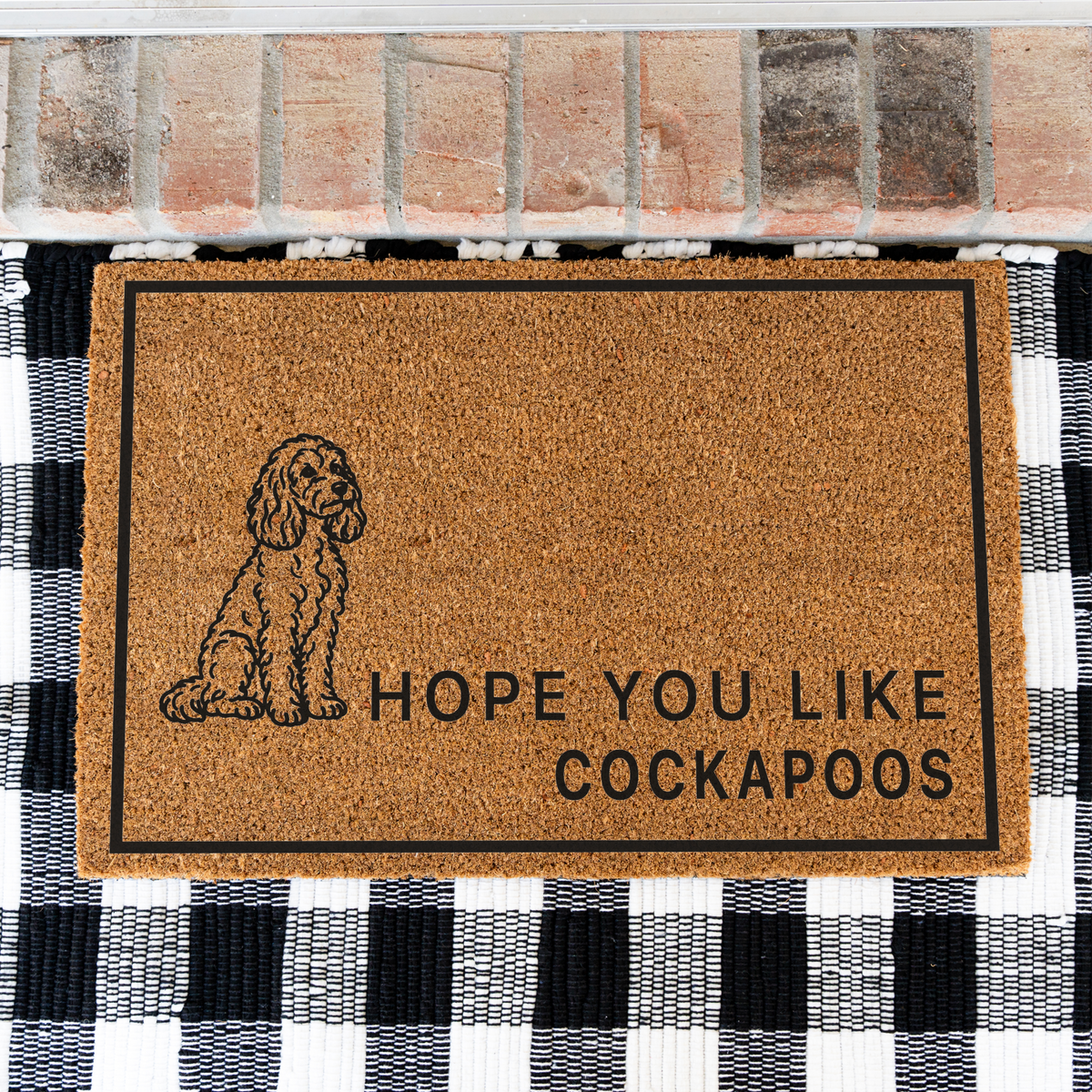 Hope You Like Cockapoos coir doormat with a drawing of a sitting Cockapoo on a black and white buffalo check rug, close view