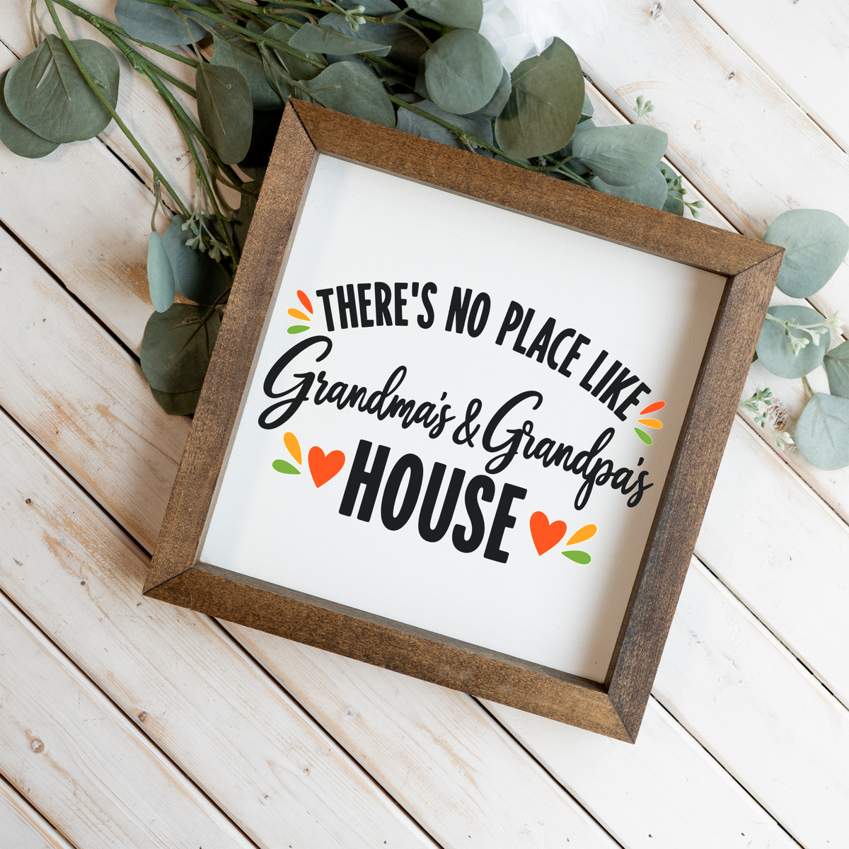 There's No Place Like Grandma's & Grandpa's House square framed sign with a walnut frame on white wood planks with eucalyptus