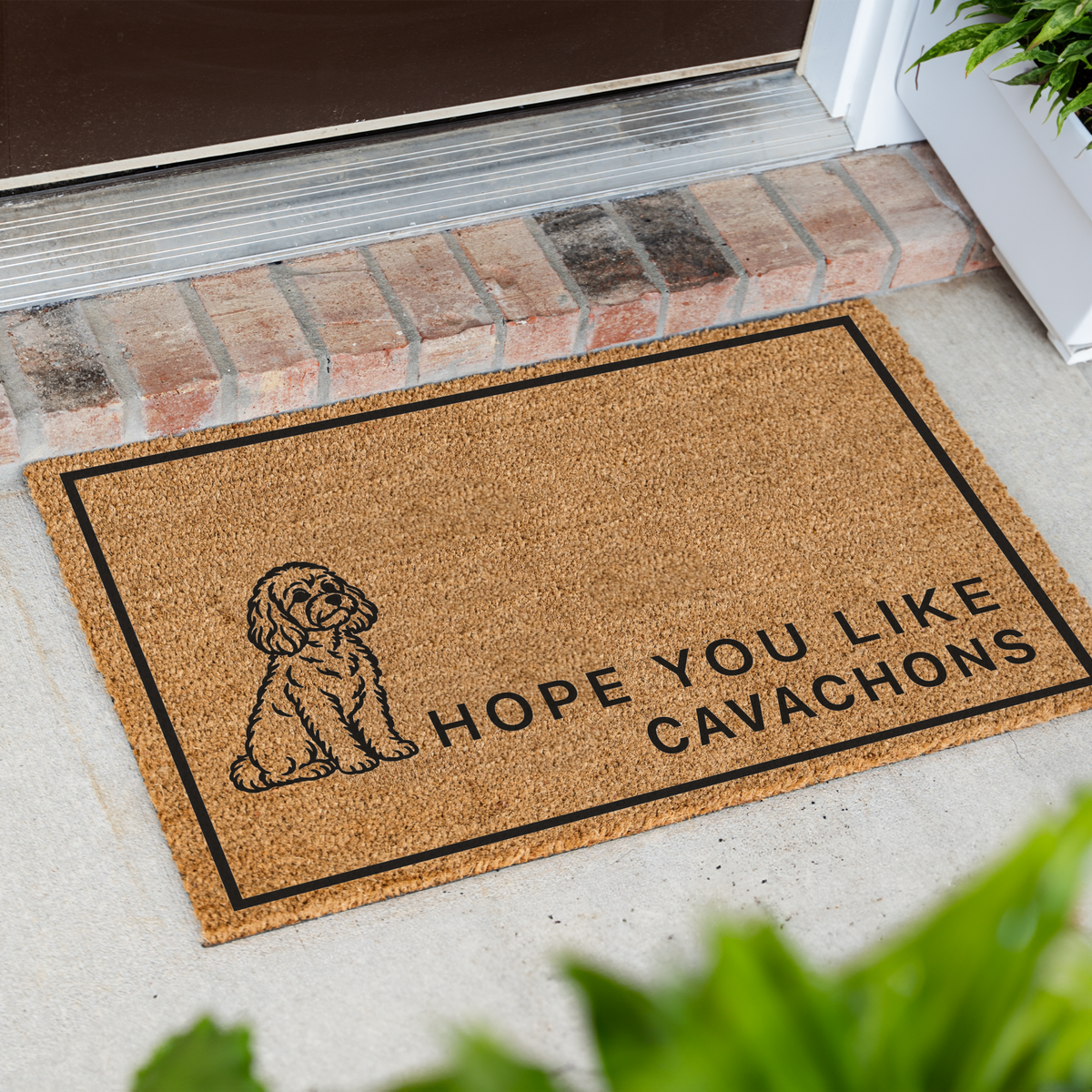 Hope You Like Cavachons coir doormat with a drawing of a sitting Cavachon at an angle on a front porch by a brick step