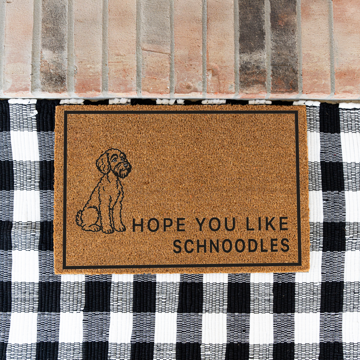 Hope You Like Schnoodles coir doormat with a drawing of a sitting Schnoodle on a black and white buffalo check rug at a brick step