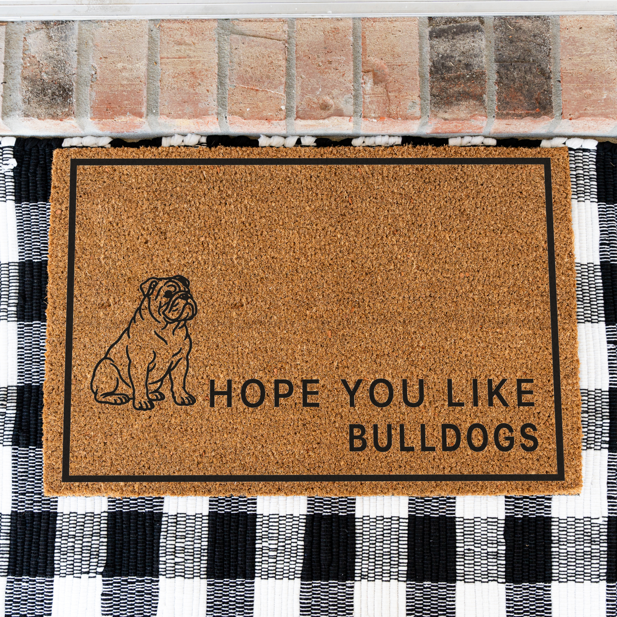 Hope You Like Bulldogs coir doormat with a drawing of a sitting bulldog on a black and white buffalo check rug, close view