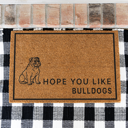 Hope You Like Bulldogs coir doormat with a drawing of a sitting bulldog on a black and white buffalo check rug, close view