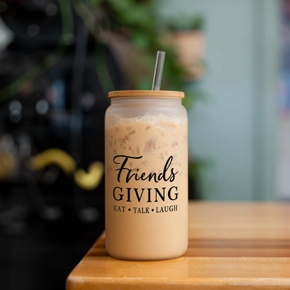 Friendsgiving 16 oz frosted glass can with a bamboo lid and straw, filled with iced coffee, on a wood table