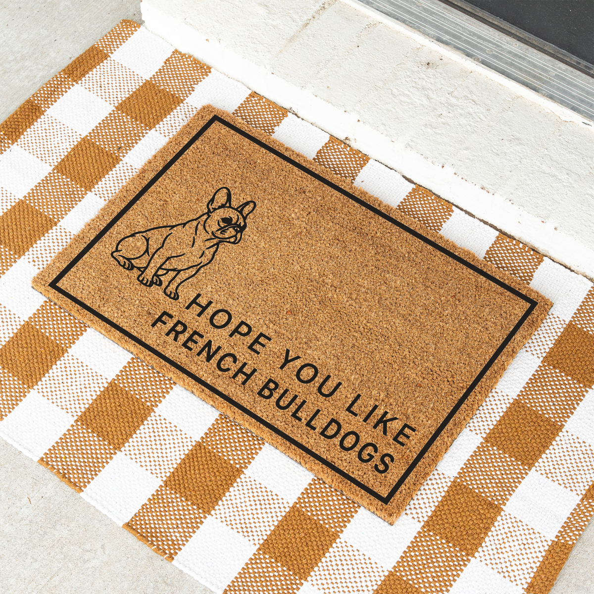 Hope You Like French Bulldogs coir doormat with a drawing of a sitting French bulldog at an angle on a tan and white check rug