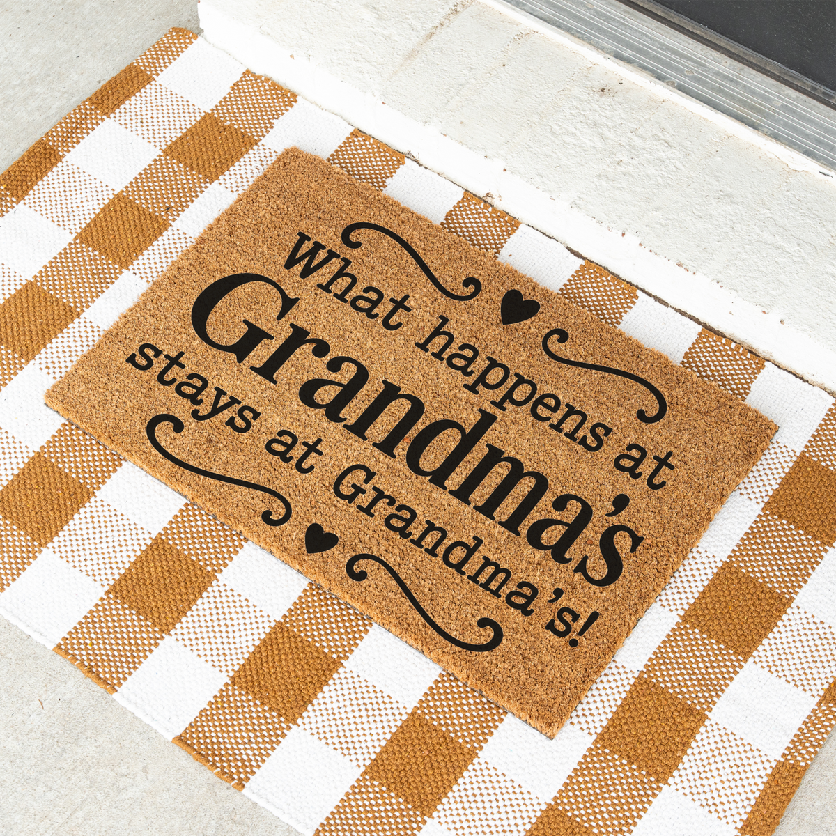 What Happens at Grandma's Stays at Grandma's coir doormat with hearts on a tan and white check rug