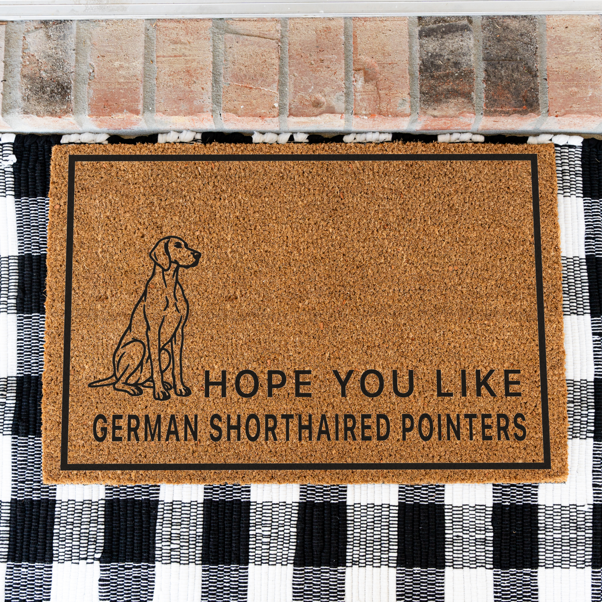 Hope You Like German Shorthaired Pointers coir doormat with a drawing of a sitting German shorthaired pointer on a black and white buffalo check rug, close view