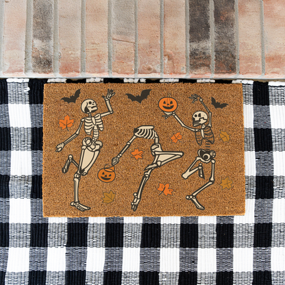Dancing skeletons Halloween coir doormat on a black and white buffalo check rug at a brick step