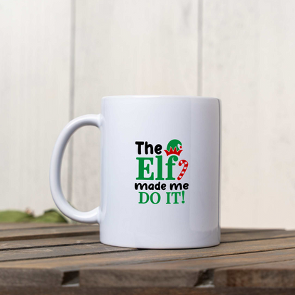 The Elf Made Me Do It white ceramic Christmas coffee mug on a wooden crate against a white wood wall