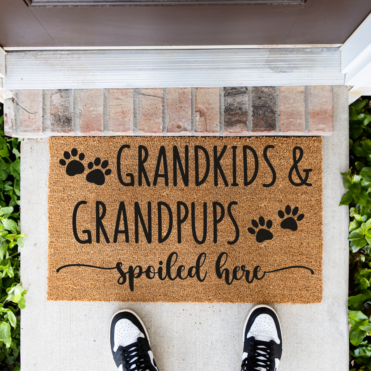 Grandkids & Grandpups Spoiled Here coir doormat with paw prints in front of a brick step, top-down view