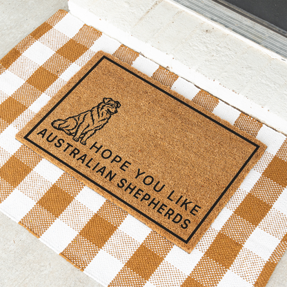 Hope You Like Australian Shepherds coir doormat with a drawing of a sitting Australian shepherd at an angle on a tan and white check rug