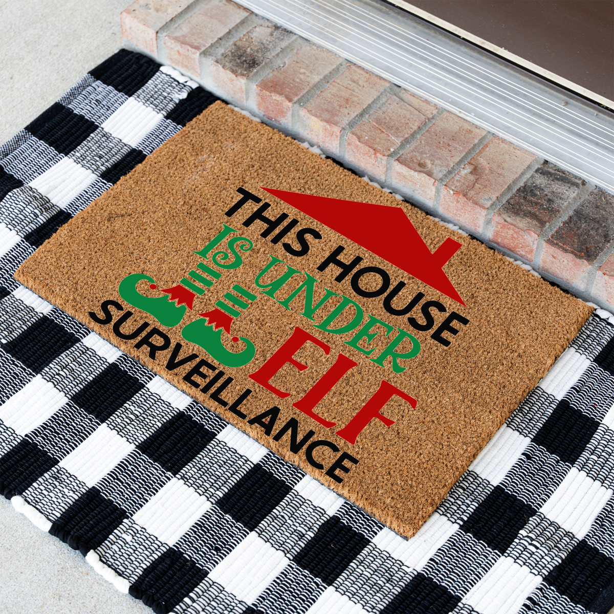 This House Is Under Elf Surveillance coir doormat at an angle on a black and white buffalo check rug