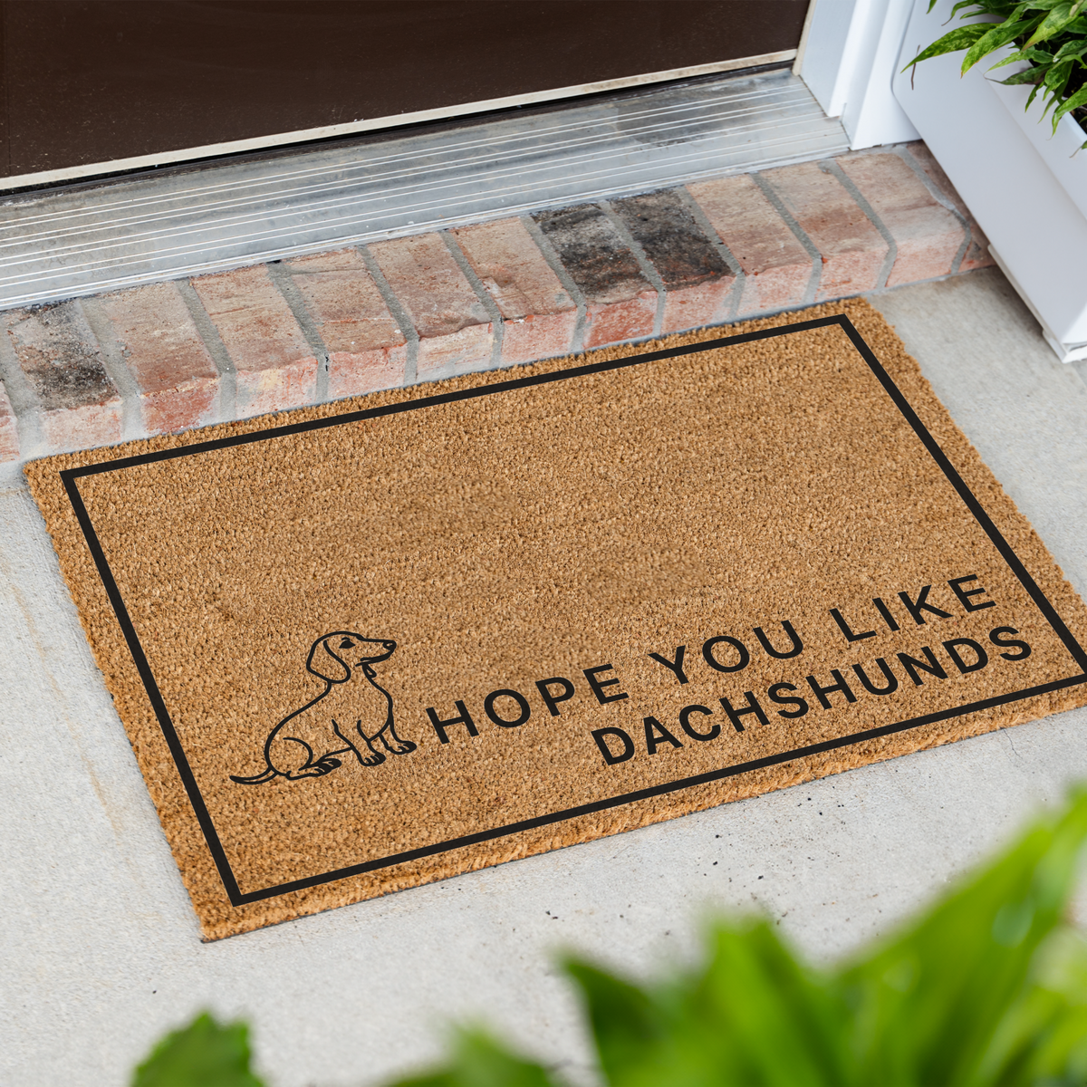 Hope You Like Dachshunds coir doormat with a drawing of a sitting dachshund at an angle on a front porch by a brick step