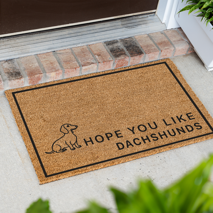 Hope You Like Dachshunds coir doormat with a drawing of a sitting dachshund at an angle on a front porch by a brick step