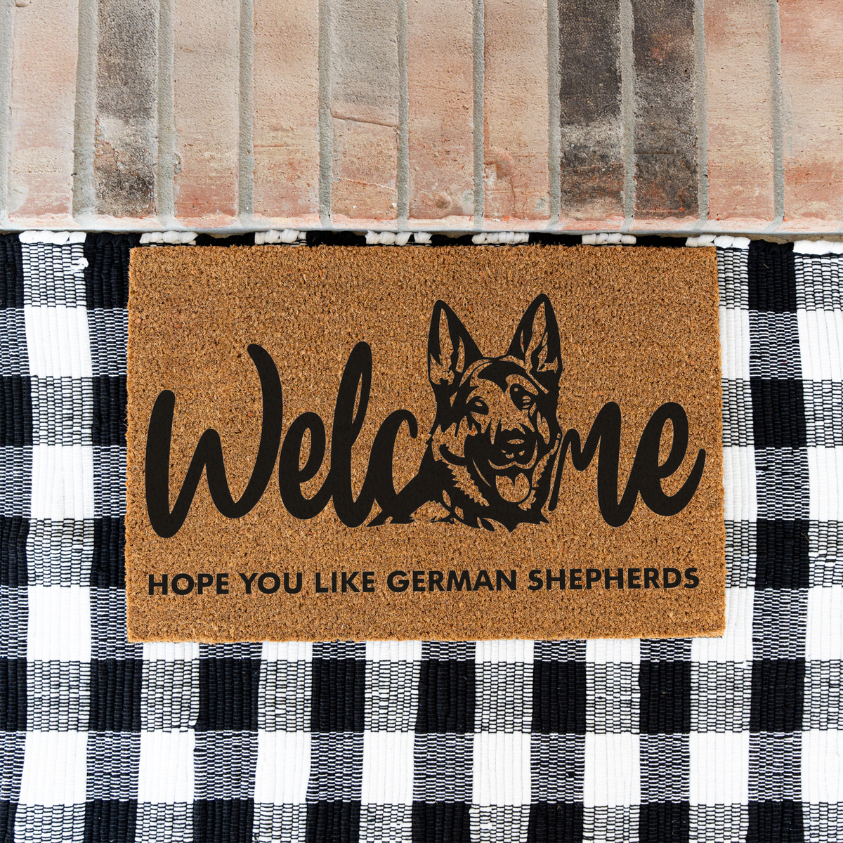 Welcome Hope You Like German Shepherds coir doormat with a German shepherd head in the word welcome on a black and white buffalo check rug at a brick step