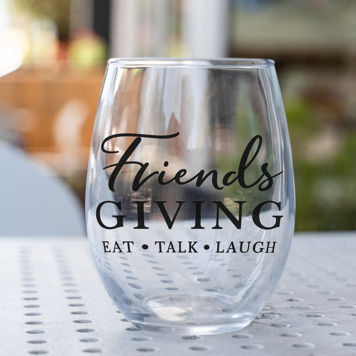 Friendsgiving stemless wine glass, empty, on a perforated metal patio table