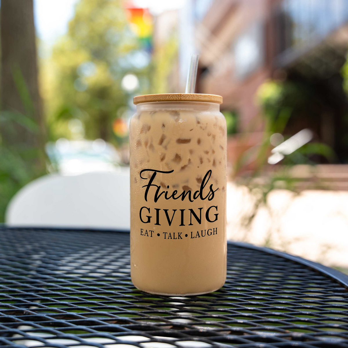 Friendsgiving 16 oz clear glass can with a bamboo lid and straw, filled with iced coffee, on a black patio table