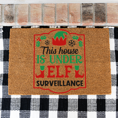 This House Is Under Elf Surveillance framed coir doormat on a black and white buffalo check rug, close view
